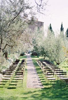 
                    
                        A gravel-covered aisle in Tuscany with simple floral-and-fern arrangements on each seat | Brides.com
                    
                